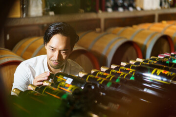 Portrait of good looking Asian man testing and examining a red wine.