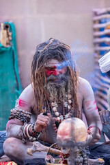 Portrait of an naga aghori sadhu holy man with pyre ash on his face and body smoking chilam at harishchandra ghat in varanasi.	