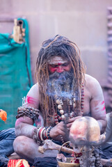 Portrait of an naga aghori sadhu holy man with pyre ash on his face and body smoking chilam at...