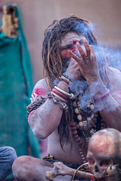 Portrait of an naga aghori sadhu holy man with pyre ash on his face and body smoking chilam at harishchandra ghat in varanasi.	