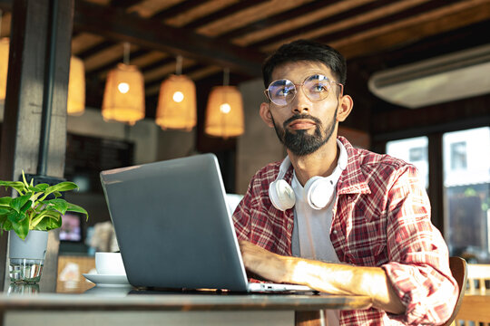 Thoughtful business man with beard in glasses looking away working on laptop computer while sitting in cafe.