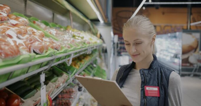 Slow motion portrait of young woman supermarket employee doing inventory checking products on shelves. Retail business and people concept.