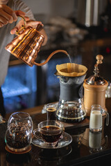 Fototapeta na wymiar drip coffee, Barista making drip coffee by pouring spills hot water on coffee ground with prepare filter from copper pot to glass transparent chrome drip maker on wooden table in cafe shop