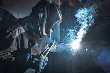 A man wearing a welding helmet is working on a piece of metal. Concept of danger and risk, as the...