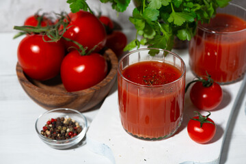 fresh tomato juice in glasses on a white background, greens and tomatoes, top view