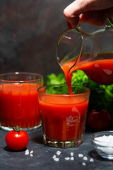 tomato juice is poured into a glass from a jug, vertical closeup