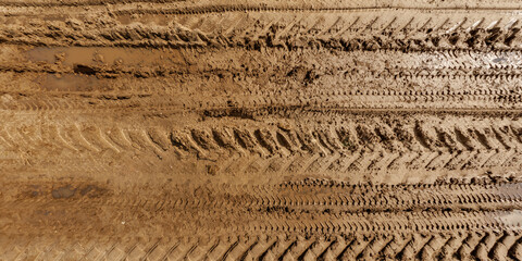 view from above on texture of wet muddy road with puddle and tractor tire tracks in countryside