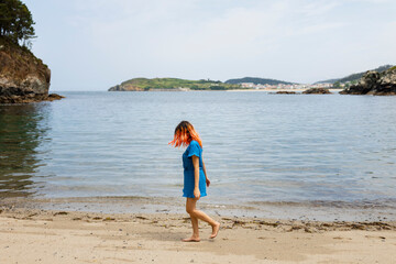 A young girl with orange hair strolls calmly along the seashore on a natural beach in northern Galicia