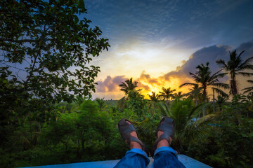 View the greenery of nature while relaxing, sitting, and showing the feet during sunset.