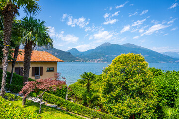 A house with a red roof sits on a hill overlooking a body of water. The house is surrounded by lush green trees and bushes, creating a serene and peaceful atmosphere, Bellagio at Lake Como, Italy - 774145521