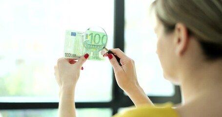 Woman looking through magnifying glass at 100 euro bill and checking authenticity closeup 4k movie slow motion. Counterfeit money concept