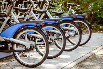 Obraz premium Bikes Sharing or e Bicycles Parking in Urban Park. Electic Bikes on Parking lot on Nature Green Background.