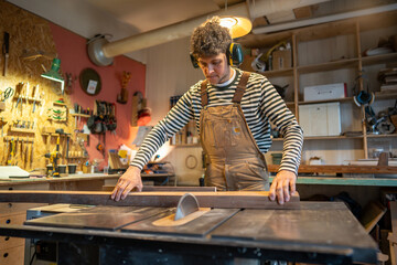 Carpentry workshop, focused craftsman master working . Thoughtful man artisan wearing earmuffs uses...