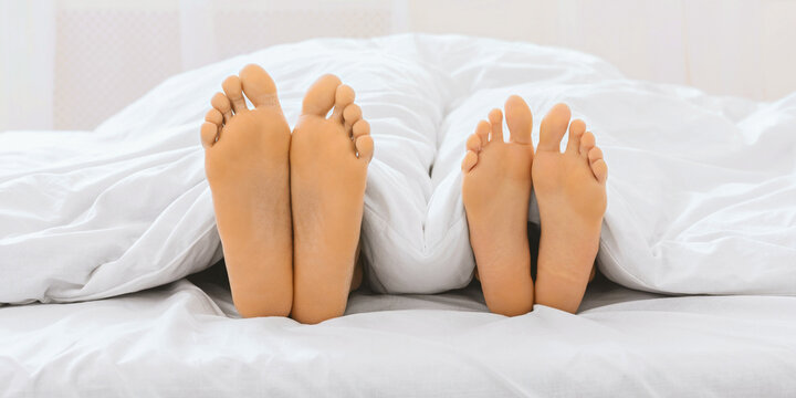 Two pairs of feet with painted toenails on bed sheets