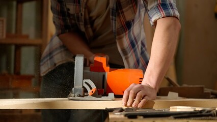 Male woodworker working in garage. Man professional carpenter specialist working with wooden materials in workshop using jigsaw, close up shot.