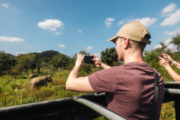 Tourist is photographing of herd of wild elephants with a smart phone. Man enjoying safari in Sri Lanka.. - 774160933