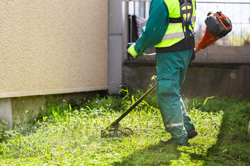 Worker trimming overgrown grass with a weed whacker - 774161170
