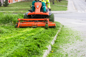 Worker mowing grass with ride-on lawn mower