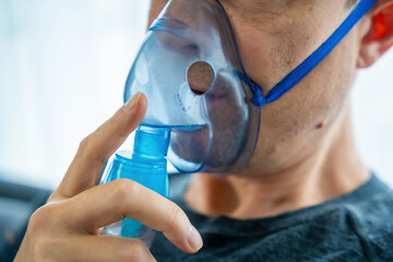Close up view of unhealthy man wearing nebulizer mask in home. Health, medical equipment and people concept - obrazy, fototapety, plakaty
