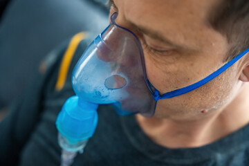 Close up view of unhealthy man wearing nebulizer mask in home. Health, medical equipment and people...