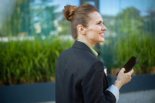 smiling female employee in business district using smartphone