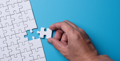 Hand holding piece of white puzzle on blue background . Business strategy teamwork and problem solving concept.