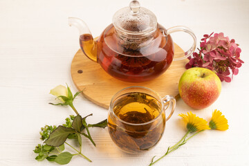 Red tea with herbs in glass teapot on white wooden. Top view.