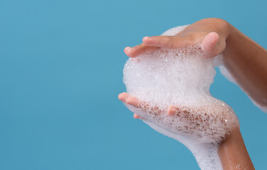 Female hand with soap bubbles on blue background. Hands with white bubbles.