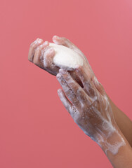Woman's hand holds a piece of soap on pink background