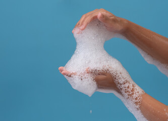 Female hand with soap bubbles on blue background. Hands with white bubbles.