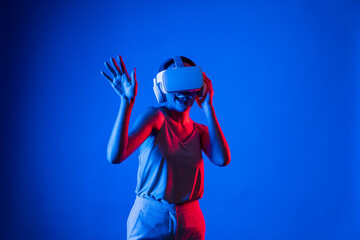 Smart female standing surrounded by neon light wearing VR headset connecting metaverse, future...