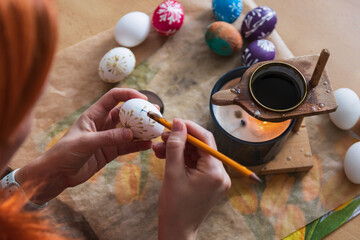 Woman hand painting easter egg with wax from candle. Traditional holiday habit, lifestyle background - 774173930