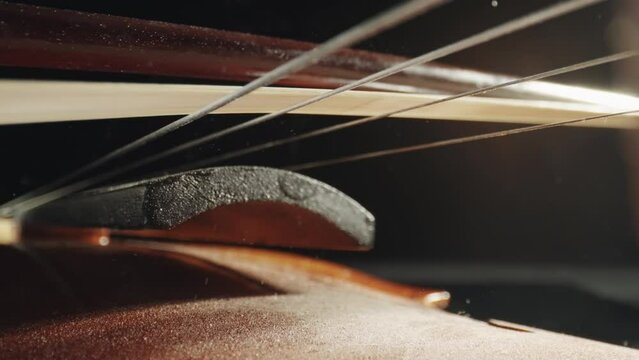 Master artisan playing with a bow on a handmade violin or cello with strings vibrating in slow motino and dust particles flying from strunes. Concept of spiritual instrument