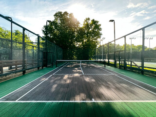 Summertime scene of elevated sport courts with nets in a public park setting. Courts are used for paddle tennis or pickleball play. Floor surface is green and blue with white boundary lines. - obrazy, fototapety, plakaty