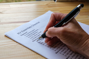 Hand holding a pen checking off boxes on RV Essentials Checklist