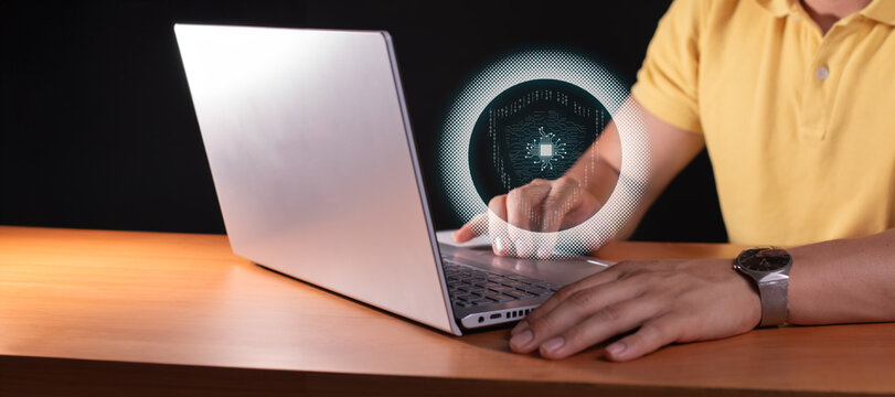 cybersecurity concept. man in yellow shirt in office black background in front of gray laptop. hologram of shield.