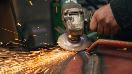 worker grinding a metal structure with sparks in a workshop - obrazy, fototapety, plakaty