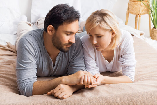 Image of closed eyes, leaned heads, holding hands man and woman, married couple, lay at bedroom, praying together before going to bed. Waiting child, pregnancy, problem issues, humility, plea concept.