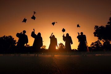 Fototapeta na wymiar silhouette cheerful graduates in black gowns Graduation hat Thrown in sunset sky