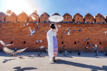 tourist woman wearing beautiful thai dress with white paper umbrella standing at Tha Phae gate...