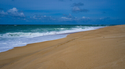 Fototapeta na wymiar Tranquil scene of waves crashing on a sandy beach under a cloud-dotted sky