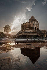 Ancient broken pagoda in Wat Chedi Luang temple reflection on water after rain at sunset