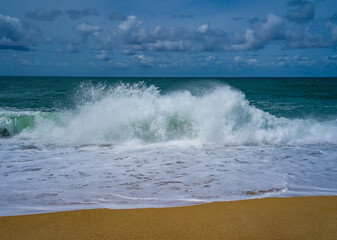 Fototapeta na wymiar Tranquil scene of waves crashing on a sandy beach under a cloud-dotted sky