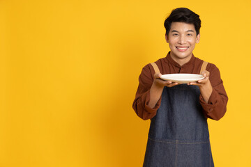 Young food waiter Asian man holding empty white plate or dish isolated on yellow background