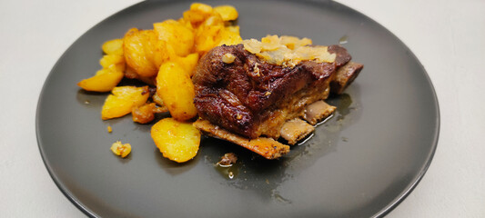 Close-up view of roasted veal ribs and fried potatoes on a dark plate

