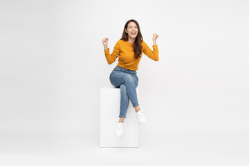Attractive beautiful Asian female sitting on white wood box and hands up raised arms from happiness, Excited woman winner success concept - 774191761