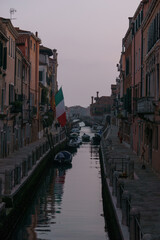 Fototapeta na wymiar Typical narrow canal surrounded by buildings with boats during evening twilight, Venice, Veneto, Italy