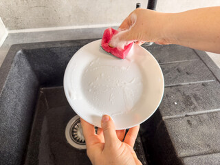 female hands washing dishes white plate in kitchen. Concept of cleaning at home