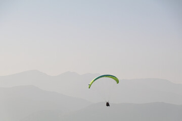 paraglider in the air with a monochrome background of a hazy mountain range in different shades of...