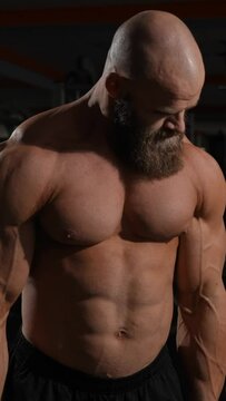 Caucasian bald topless man doing an exercise with a barbell in the gym. Bicep curls with weights. Vertical video. 